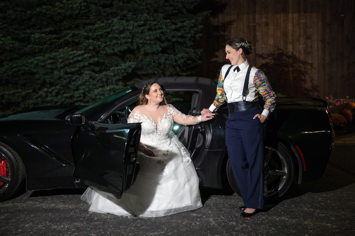 A man and woman holding hands in front of a car.