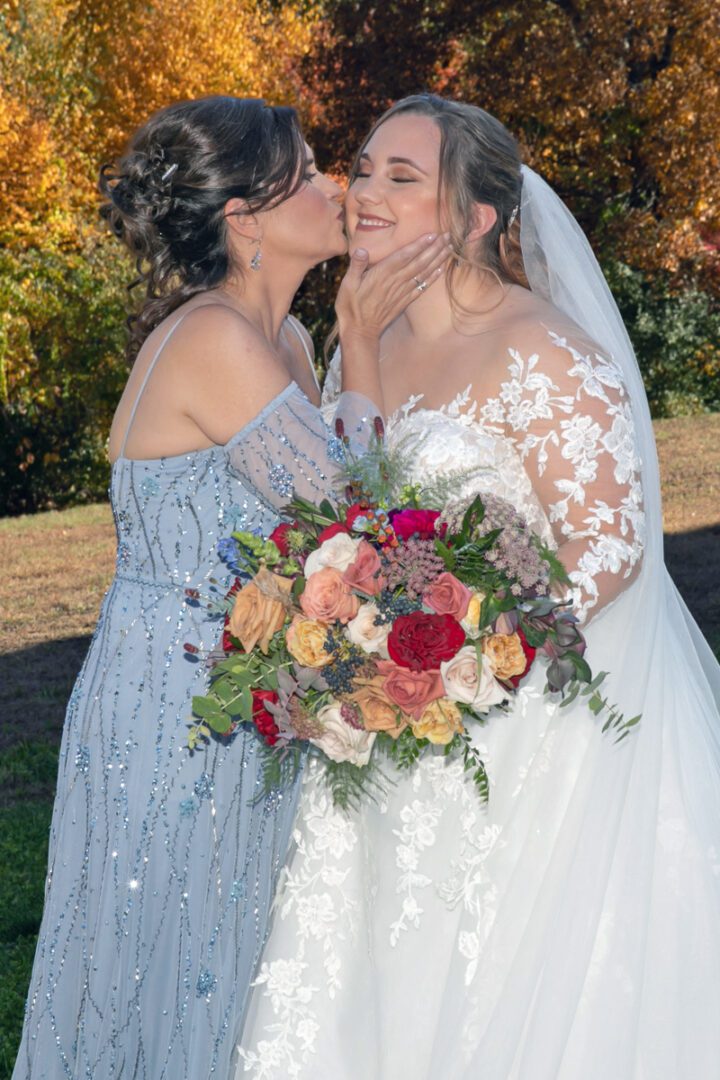 Two women kissing each other while holding a bouquet of flowers.