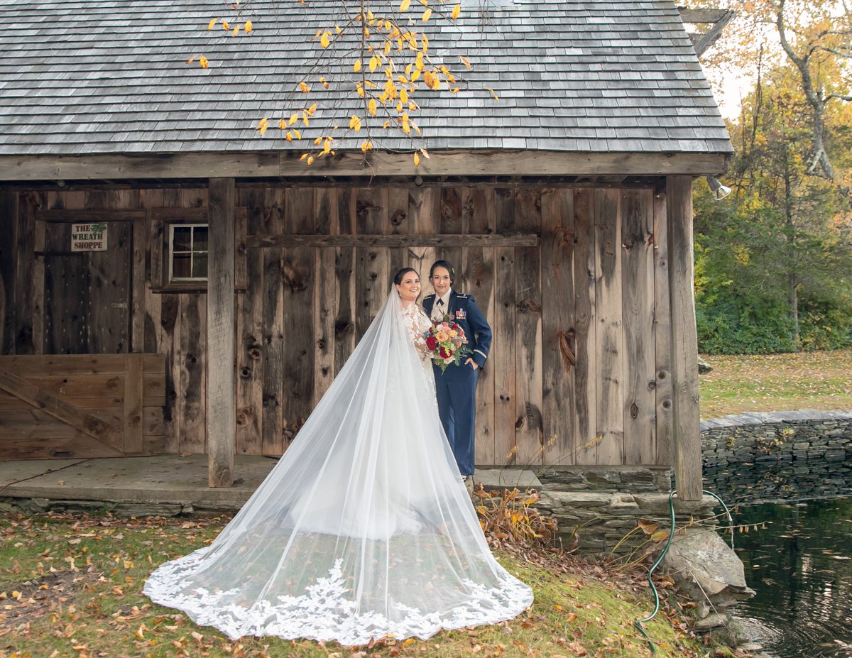 A bride and groom pose for a picture outside of their barn.